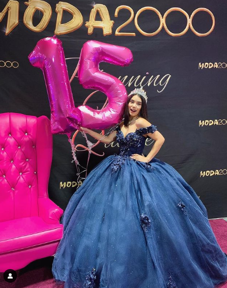 A woman in a blue Quinceanera gown standing next to a pink chair