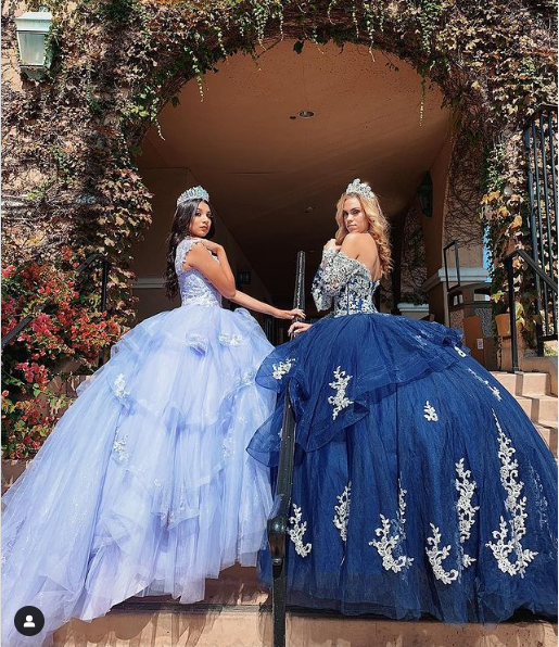 Two women in blue Quinceañera dresses sitting on steps in gown