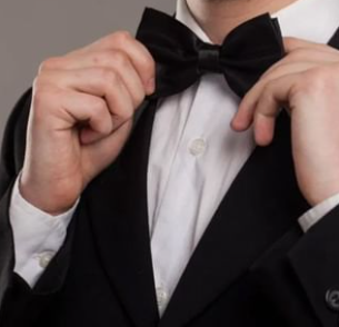 A man in a tuxedo adjusts his bow tie, with a Quinceanera theme