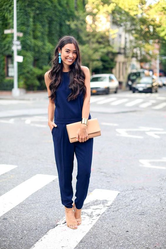 A woman wearing a navy blue jumpsuit and holding a clutch, providing outfit ideas for Quinceanera
