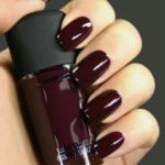 A person holding a bottle of dark wine nail polish