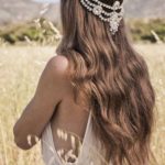 Quinceanera: A woman with boho chic bridal hairstyles wearing hair jewellery, standing in a field of tall grass