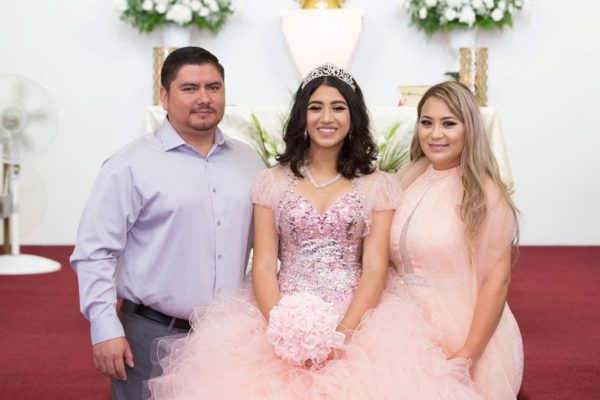 A Quinceanera party with a man and two women standing in a church wearing a Quinceanera gown