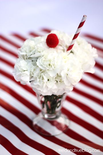 A Quinceanera themed image featuring a vase filled with white flowers, a red and white striped table cloth, and whipped cream Ice Cream.