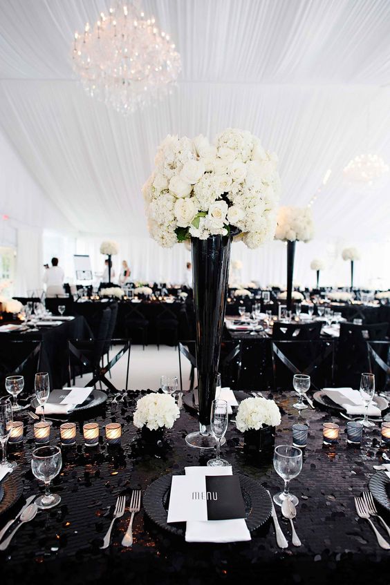 Quinceanera ideas - A black wedding theme featuring a black table adorned with white flowers and place settings
