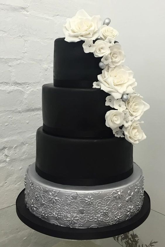 A pastel Quinceanera cake with a black and silver design adorned with white flowers