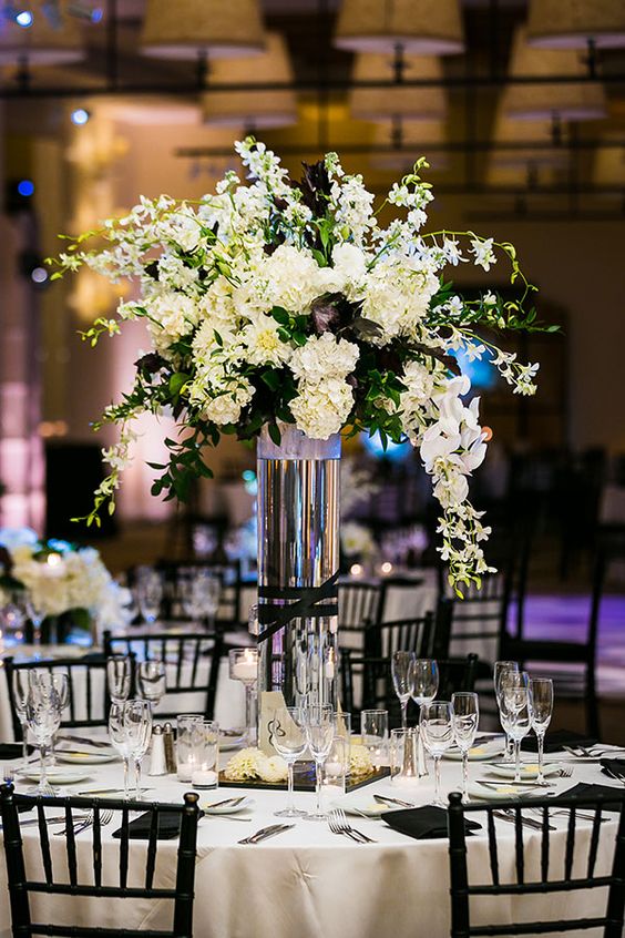 A black and white Quinceanera centerpiece featuring a tall vase filled with white flowers on top of a table.