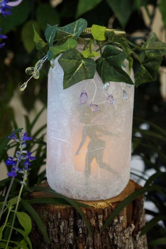A Quinceanera-themed image featuring a mason jar Tinker Bell and a candle sitting on a tree stump.