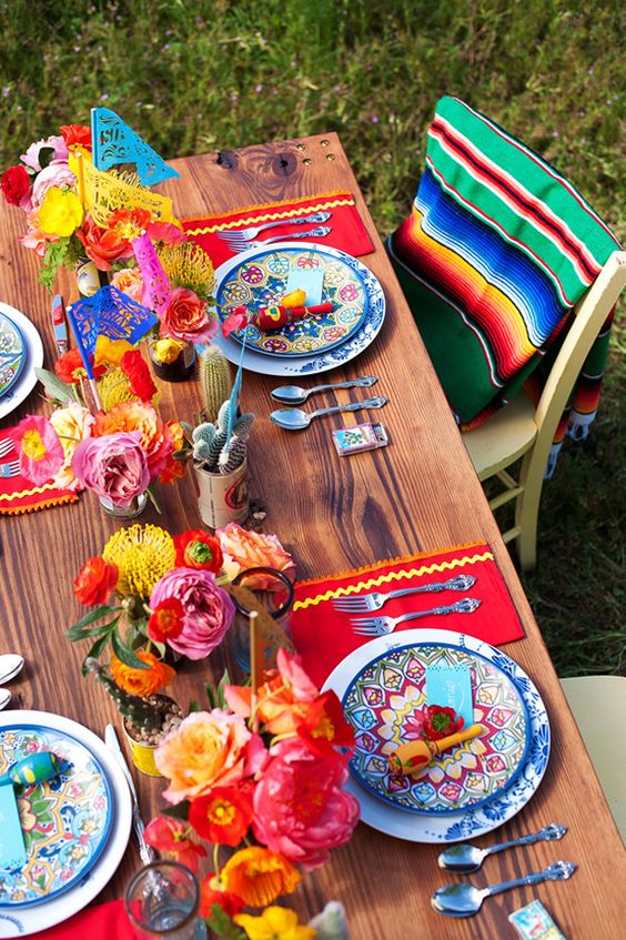 Quinceanera image of a Mexican table setup, featuring a wooden table topped with colorful plates and flowers