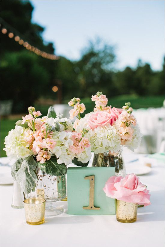A Quinceanera table topped with vases filled with flowers in a wedding color theme
