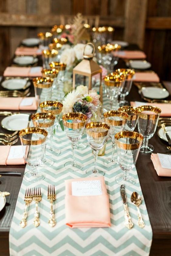 A long table set with salmon and gold decorations for a Quinceanera celebration, with place settings arranged beautifully