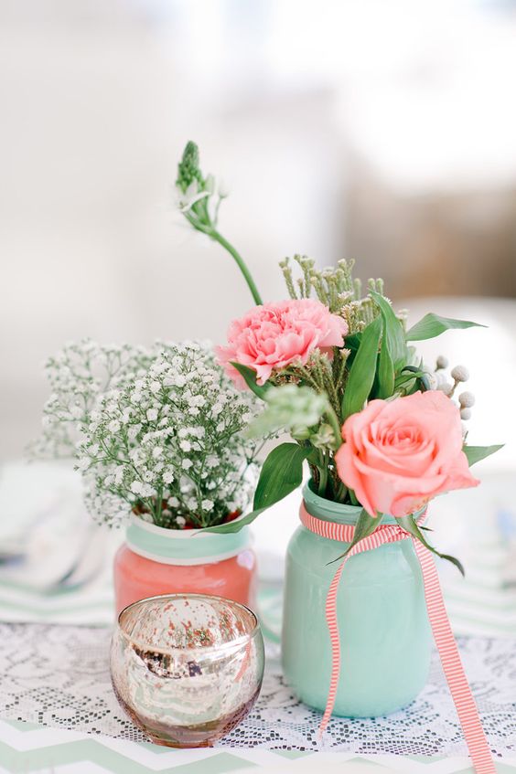 Quinceanera invitation featuring coral and mint color palette. Two vases with flowers displayed on a table.