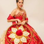 A woman in a red and gold Quinceañera gown holding a fan
