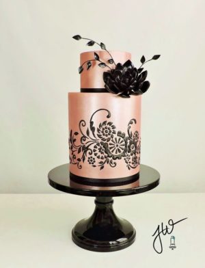 A Quinceanera cake with a black and rose gold design and pink flowers on top