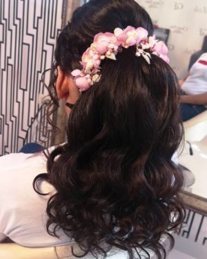 A woman with black hair wearing a Quinceanera hairstyle, with a flower in her hair