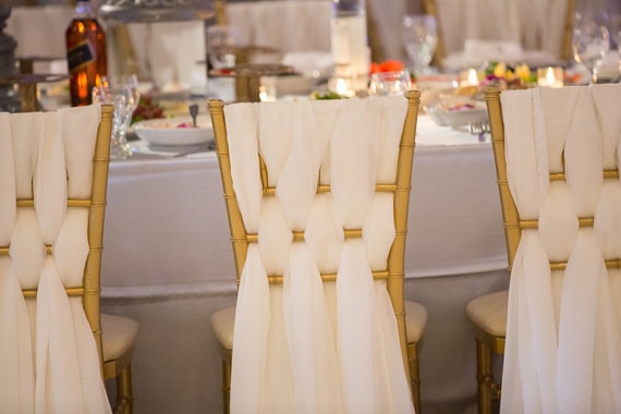 A close up of a table with many chairs decorated with Quinceanera chiavari chair sashes