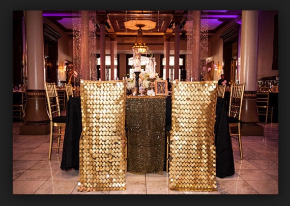 A Quinceanera function hall with a table adorned with gold chairs and a black tablecloth.