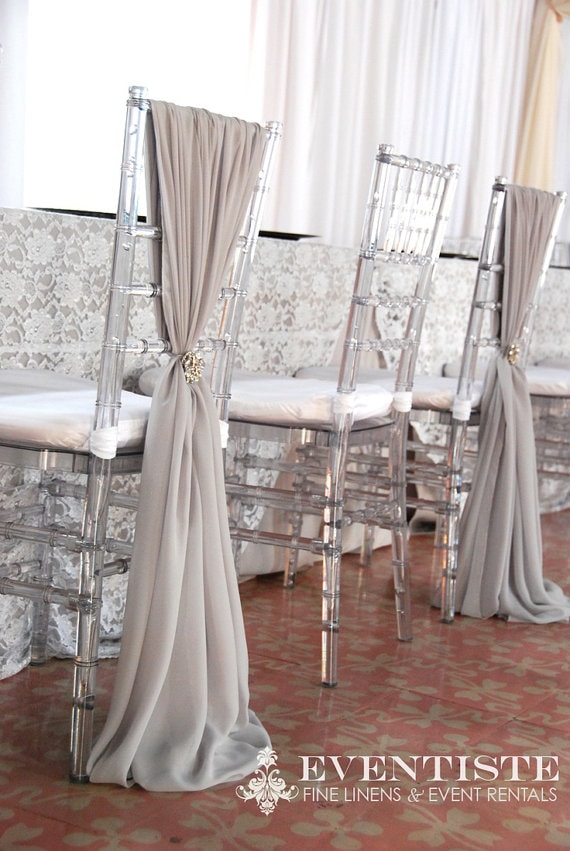 Clear chivari chairs with sash arranged around a table, with a row of chairs behind covered by a curtain draped over them - Quinceanera