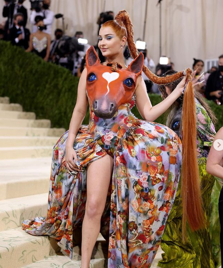 A woman with long hair sitting on a staircase wearing an ugly Quinceanera dress by Stella McCartney at the Met Gala