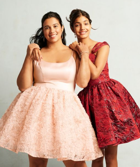 Two women standing next to each other in Quinceanera dresses, with a fashion model dress.