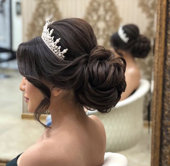A woman getting her hair done in a salon for a Quinceanera, wearing a headpiece bun.