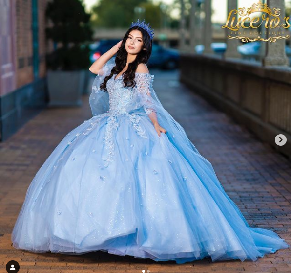 A woman in a light blue Quinceanera dress with a cape, posing for a picture