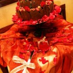 A beautiful Quinceanera cake with chocolate torte color and stunning red flower decorations on a table