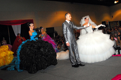 A man and woman in traditional Quinceanera attire, the man wearing a suit and the woman wearing a fashionably elegant gown