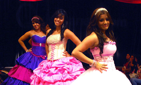 A group of women standing next to each other on a stage, wearing performance Quinceañera dresses