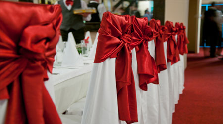 A flower table with a row of white tables covered in red bows