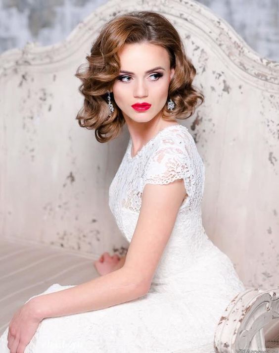 A woman in a white dress sitting on a couch with short hair styled in curls for a Quinceanera celebration.