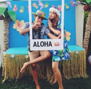 A Quinceanera photo booth with a Hawaiian theme. A man and a woman sitting on a bench.