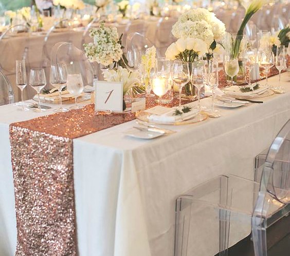 A beautiful Quinceanera table setup with a rose gold sequin table runner. The long table is adorned with a number of place settings.