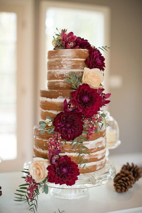 A Quinceanera cake with a rustic touch. The three tiered cake is adorned with flowers and pine cones.