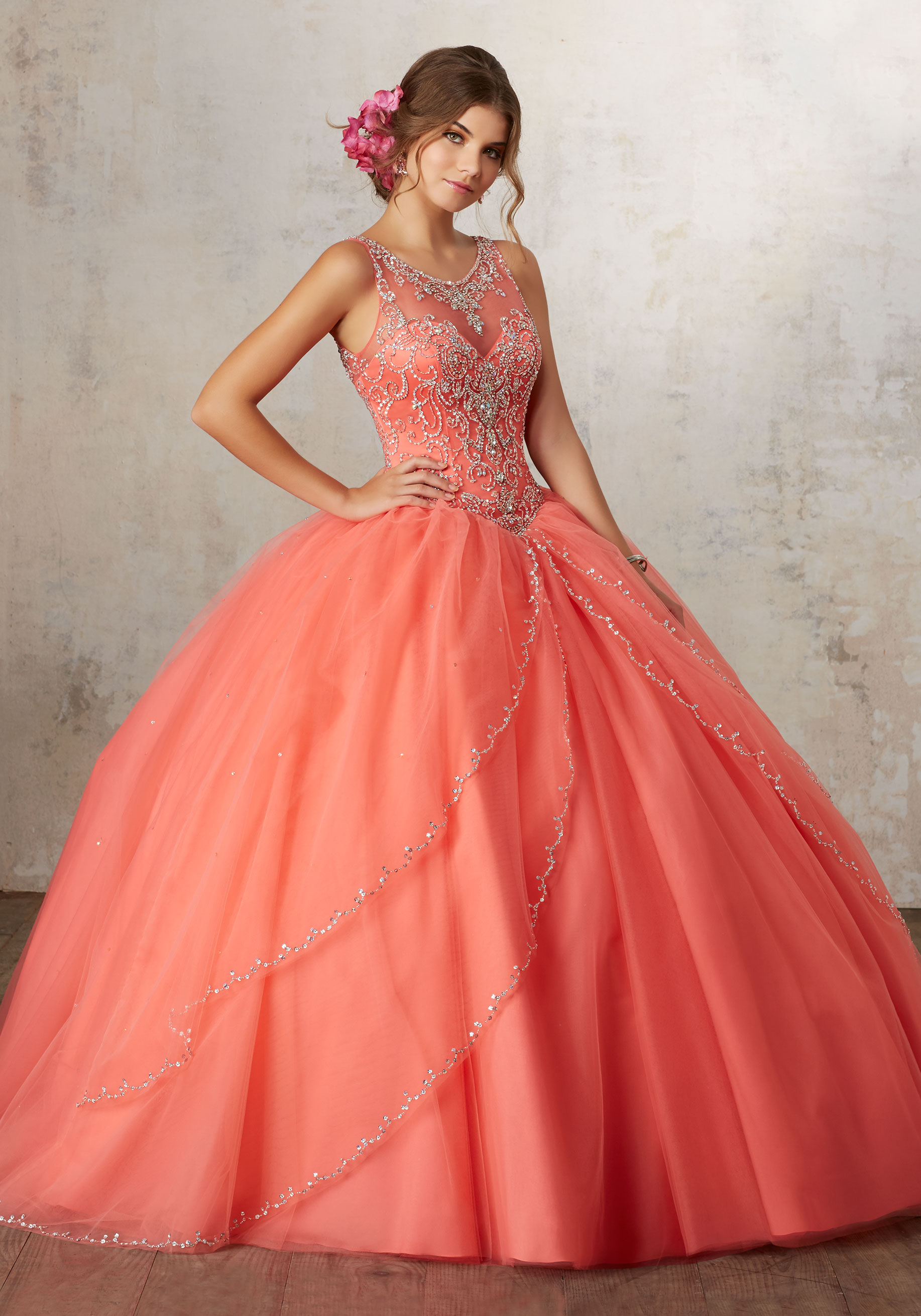A woman in a coral Quinceañera dress posing for a picture in a ball gown