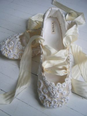 A pair of ivory slipper shoes with a ribbon tied around them, perfect for a Quinceanera