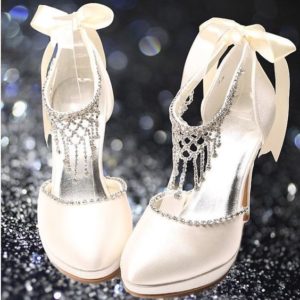 A pair of white slipper-style high heeled footwear with bows on them, suitable for a Quinceanera event.
