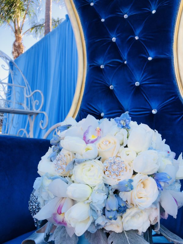 A beautiful floral design with a bouquet of white and blue flowers arranged on a blue chair for a Quinceanera celebration.