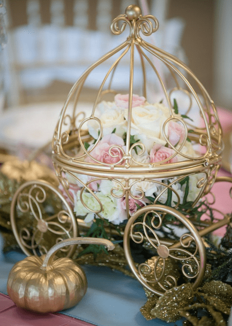 A Quinceanera party with a Cinderella theme. A gold carriage with flowers in it on a table.