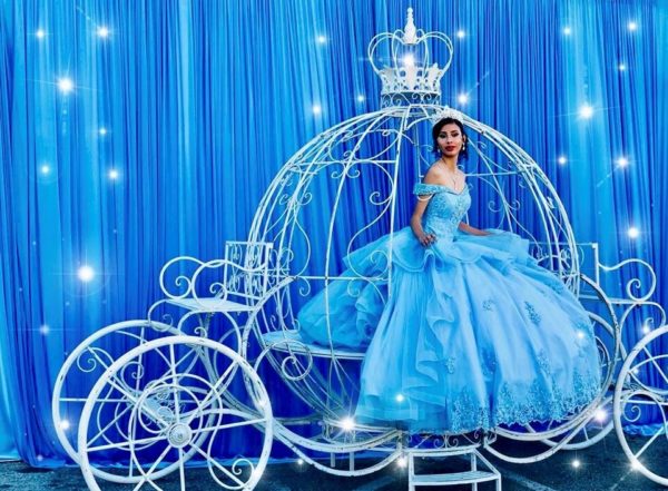 Quinceañera in a blue dress sitting in a white carriage with a Cinderella theme