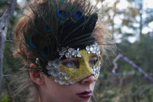 A woman wearing a carnival headpiece and a mask with feathers on her head for a Quinceanera celebration