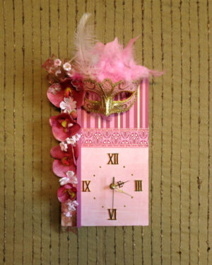 A pink Quinceanera clock with a mask resting on top, surrounded by petals.