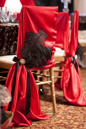 Decorated chairs and table for a Quinceanera celebration, featuring a chair covered in red cloth and a black feather