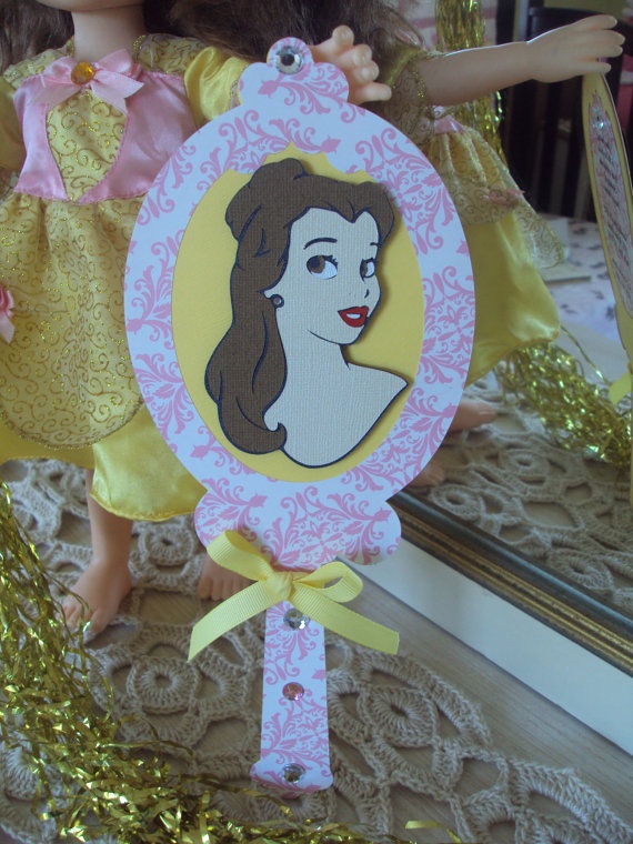 A Quinceañera doll holding a mirror with a picture of a princess from tarjetas de la bella y la bestia.