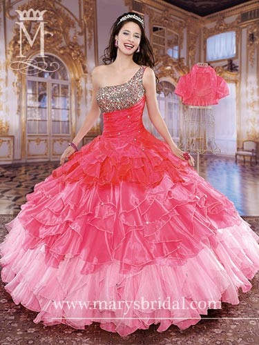 A shoulder Quinceañera standing near a table topped with a Quinceañera cake covered in pink and green paper fans
