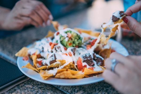 A Quinceanera themed image featuring Latin American cuisine. The image shows a white plate topped with nachos covered in cheese.