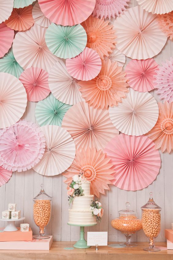 A shoulder Quinceañera standing near a table topped with a Quinceañera cake covered in pink and green paper fans