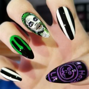 A person with a Quinceanera themed manicure. The nails feature black and white designs with green accents.