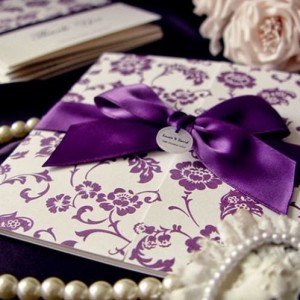 A Quinceanera invitation featuring lilac colors and a purple ribbon