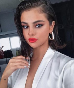 Selena Gomez, a woman wearing a white robe and red lipstick with a wet look hairstyle for a Quinceanera